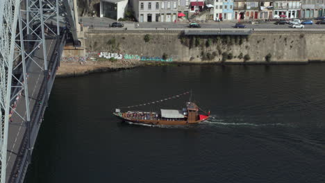 Scenic-shot-of-a-boat-gliding-towards-the-bridge-in-Porto