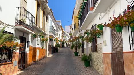 Caminando-Por-El-Casco-Antiguo-De-Estepona-En-Una-Típica-Calle-Estrecha-Española-Con-Casas,-Coloridas-Macetas-Y-Hermosos-Balcones,-Día-Soleado-En-Andalucía-España,-Toma-De-4k