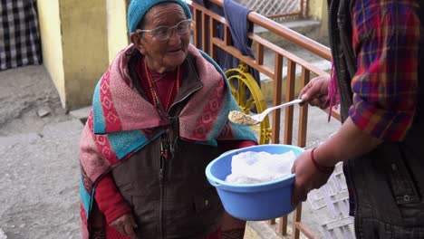 In-Spiti-Oder-Kaza,-Einem-Abgelegenen-Dorf-Nahe-Der-Indochinesischen-Grenze,-Lächelt-Eine-Alte-Tibetische-Dame-Eine-Person-An,-Während-Essen-In-Ihre-Schüssel-Serviert-Wird