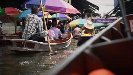 Helmsman-rowing-the-passenger-boat-using-paddle-through-the-canal-in-Bangkok,-Thailand-jib-shot