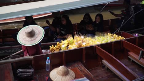 Local-vendor-selling-fruits-to-passing-tourists-in-canal-at-Damnoen-Saduak-Floating-Market-in-Ratchaburi,-Thailand,-static-closeup