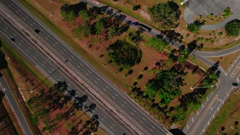 Aerial-perspective-of-a-bustling-multi-lane-highway-adjacent-to-a-green-park-area-with-scattered-trees-and-pathways