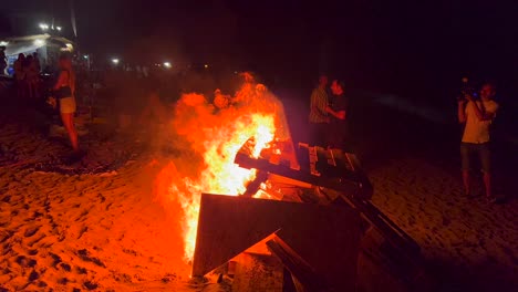 People-at-traditional-bonfire-summer-festival-at-the-beach-at-the-San-Juan-celebration-in-Marbella-Spain,-enjoying-a-fun-party,-big-burning-fire-and-hot-flames-at-night,-4K-shot