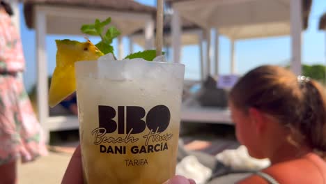 Enjoying-a-delicious-summer-fruity-cocktail-with-friends-in-Bibo-Beach-House-Tarifa-restaurant,-blurry-people-having-fun-in-restaurant-of-Dani-Garcia-in-Spain,-4K-static-shot