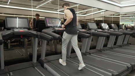 Sportsman-guy-runs-on-treadmill-and-watch-music-video-on-tv-in-modern-gym