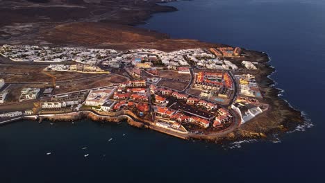 Picturesque-aerial,-Town-with-houses-and-windmills-at-coast-and-boats-at-island-tenerife-during-golden-hour-evening-summer-sun