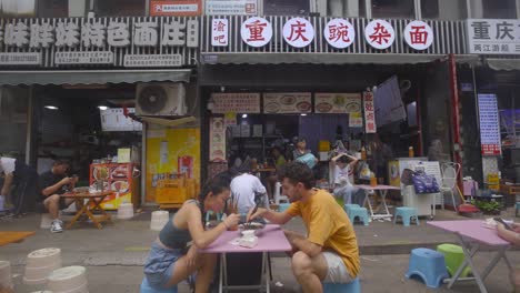 White-man-and-asian-woman-sit-down-to-share-a-bowl-of-noodles-at-street-market
