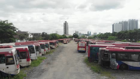 Low-flying-over-old-abandoned-busses-at-junkyard-at-Kuala-lumpur,-aerial