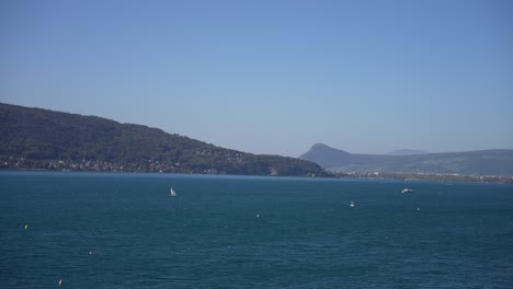 Sailboats-on-Lake-Annecy-in-the-French-Alps-on-a-sunny-day,-Wide-pan-right-shot