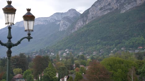 Mountain-village-of-Annecy-in-the-French-Alps-with-rocky-hills-behind-and-streetlight-left,-Stable-wide-shot