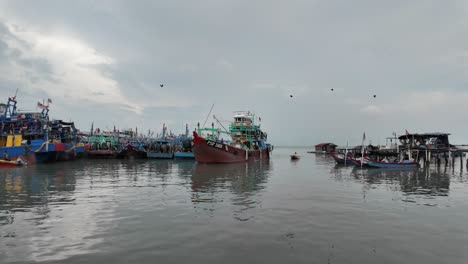 Vibrant-coastal-harbor-with-colorful-fishing-boats,-and-the-Malaysian-flag-indicating-location-against-an-overcast-sky