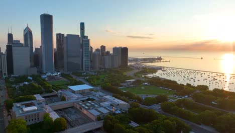 Downtown-Chicago-Millennium-Park-Im-Morgengrauen:-Wolkenkratzer-Ragen-über-Grünem-Gelände-Empor,-Auf-Dem-Wasser-Spiegeln-Sich-Die-Hafenboote-Und-Ein-Goldener-Sonnenaufgang