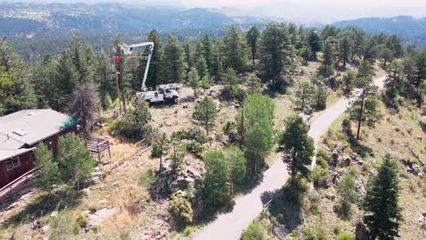 Aerial-view-rotating-around-a-bucket-truck-as-a-utility-crew-works-on-a-power-pole-on-the-top-of-a-ridge-in-a-remote-mountain-neighborhood