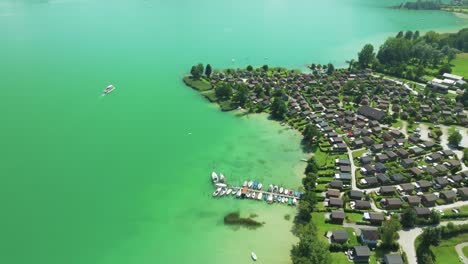 Fesselnde-Luftaufnahme-Des-Ruhigen-Smaragdgrünen-Wassers-Von-Mondsee,-Die-Den-Blick-Auf-Ein-Luxuriöses-Dorf-Am-Seeufer-Und-Gemütliche-Boote-Freigibt,-Eine-Perfekte-österreichische-Urlaubsszene