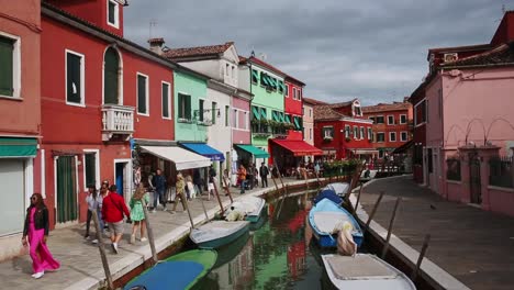 Busy-sidewalks-by-traditional-canal-and-colourful-buildings-in-Burano,-Venice,-Italy