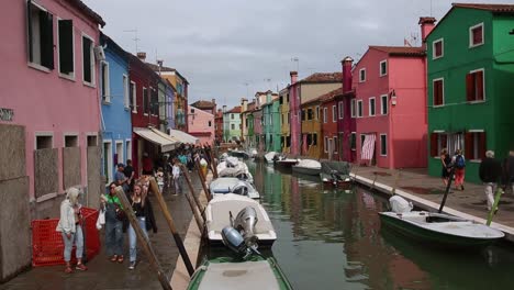 Tourists-walk-by-traditional-colourful-houses-and-canal-in-Burano,-Venice,-Italy