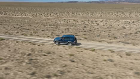 Un-Vehículo-En-Rápido-Movimiento-Corriendo-Por-El-Desierto-Cerca-Del-Parque-Nacional-Del-Cañón-Charyn-En-Kazajstán,-Asia-Central---Toma-Aérea-De-Seguimiento