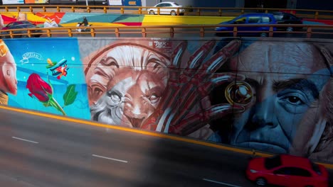 aerial-view-street-art-mural-on-Mexico-city-highway-colorful-painting-old-man-hand-bones-lion-rose-airplane-kid-crown-cars-passing-fast