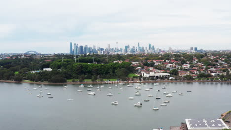 Aerial-drone-shot-flying-over-the-parramatta-river-towards-the-Sydney-city-skyline-and-harbour-bridge-in-the-distance,-Australia