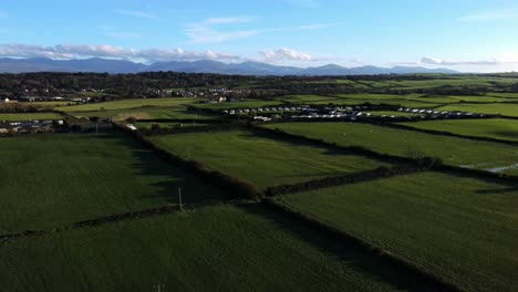 Sunset-shadows-aerial-view-over-patchwork-Anglesey-farmland-meadows-under-Snowdonia-mountain-range