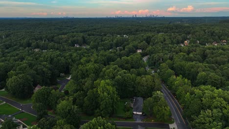 Drone-flight-over-green-suburb-area-of-Atlanta-with-road-between-green-trees-at-sunset,-Georgia
