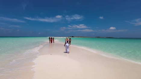 Rearview-shot-of-a-group-people-walking-on-white-sand-beach-while-looking-out-sandbar,-cayo-de-Agua