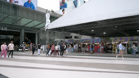 La-Gente-Está-Ocupada-Caminando-Fuera-De-Siam-Paragon-En-Bangkok-Con-La-Estación-De-Tren-BTS-Con-Trenes-Que-Salen-Y-Paran-Para-Pasajeros,-En-Tailandia