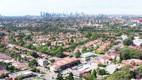 Aerial-drone-shot-flying-over-residential-houses-towards-Sydney-city-in-the-distance,-Australia