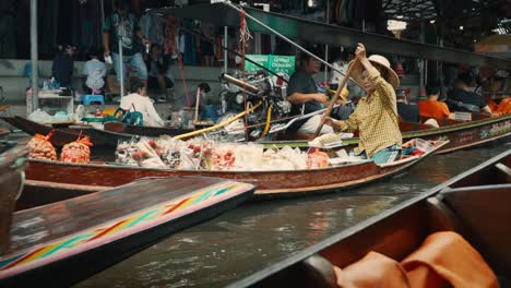 Una-Anciana-Lucha-Por-Remar-Sus-Mercancías-Entre-Botes-Motorizados-De-Cola-Larga-En-Un-Canal