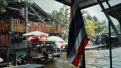 Die-Thailändische-Flagge-Hängt-Auf-Dem-Schwimmenden-Markt-Damnoen-Saduak,-Während-überdachte-Langheckboote-Touristen-Befördern