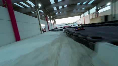 FPV-Renndrohne-Fliegt-über-Piloten,-Die-Schnelle-Go-Karts-Auf-Der-Indoor--Und-Outdoor-Strecke-Des-Kartdrome-In-Italien-Fahren