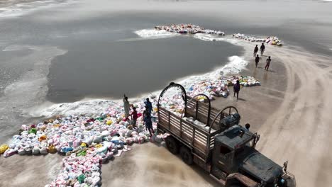 Aerial-drone-rotating-shot-over-salt-lake-in-Sanghar,-Sindh-in-Pakistan-with-locals-collecting-bags-of-salt-on-a-truck-at-daytime