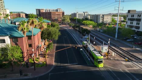 Sunlit-Tempe,-Arizona-street-with-palm-trees,-multi-story-buildings,-and-a-green-tram-gliding-on-rails