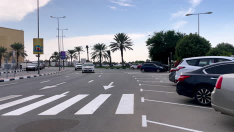 Autos-Circulando-Por-Una-Calle-De-La-Ciudad,-Estacionamiento-Con-Muchos-Autos-En-Filas,-Dubai,-Emiratos-Árabes-Unidos-4k