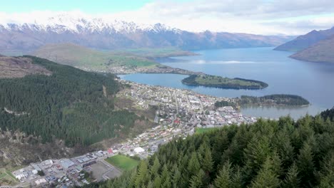 Aerial-view-of-Queenstown,-revealing-over-trees-to-lake-and-mountain-scenery,-New-Zealand
