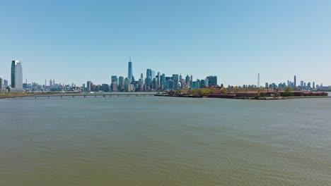 Aerial-approaching-shot-of-Ellis-Island-with-bridge-and-New-York-Skyline-in-background