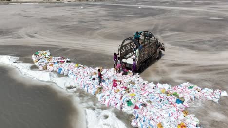 Aerial-drone-top-down-shot-over-labourers-lifting-salt-bags-after-collection-from-salt-lake-Sanghar,-Sindh,-Pakistan-on-a-bright-sunny-day