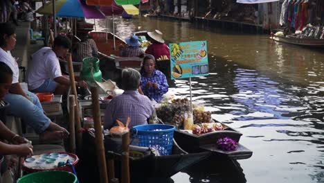 Sellers-gathered-canalside,-talking-to-each-other,-as-boats-move-in-the-canal