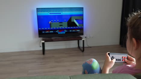 Kleinkind-Spielt-Abends-Mit-Einer-Vintage-Spielekonsole,-Bewegte-Filmaufnahme,-Fernseher-Mit-Einem-Spiel-Im-Hintergrund