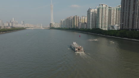 Aerial-follow-shot-of-a-ferry-boat-on-the-river-in-downtown-Guangzhou-city,-China