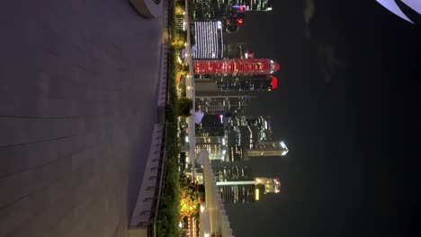 Mesmerizing-vertical-footage-captures-a-nocturnal-stroll-around-Marina-Bay-Sands,-where-luminous-skyscrapers-adorn-the-dazzling-cityscape,-creating-an-awe-inspiring-spectacle