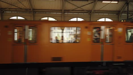 Öffentliche-Verkehrsmittel-In-Berlin-Kreuzberg-Mit-Orangefarbenem-Zug,-Der-Den-Bahnhof-Verlässt