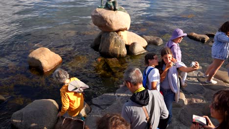 Little-Mermaid-statue-on-rock-in-water-with-many-people-taking-pictures-in-Copenhagen,-Denmark