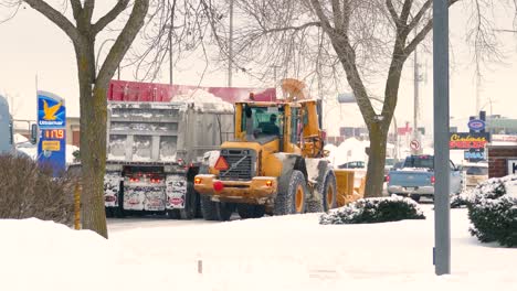 Excavator-with-plow-blows-snow-into-truck-trailer,-road-cleaning-and-maintenance-in-Montreal,-Canada