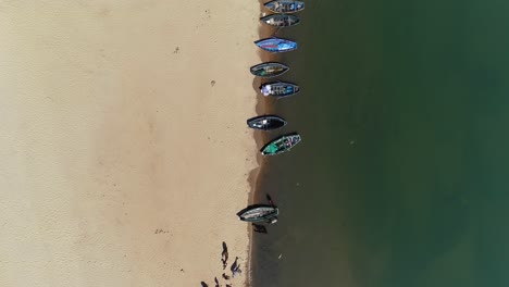 A-stunning-aerial-view-of-boats-docked-by-the-beach,-showcasing-a-vivid-contrast-between-the-golden-sands-and-the-glistening-waters