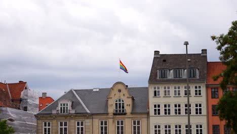 Colorful-flag-on-top-of-building-representing-LGTBI-community-waving-in-wind-in-Copenhagen,-Denmark