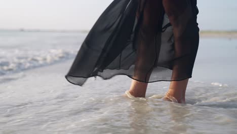 Up-close-waves-crashing-on-latina-women-feet-with-black-dress-in-Coche-island,-Venezuela-in-lsow-motion