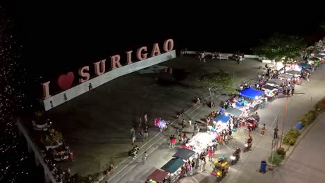 Surigao-City-Boulevard-on-a-busy-night,-showing-large-'I-Love-Surigao'-sign,-in-a-night-time-aerial-drone-shot