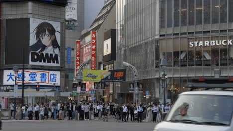 Multitud-De-Personas-Esperando-En-Shibuya-Cruzando-Tokio-Japón,-Autos-Circulando