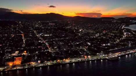 A-bright-orange-sunset-over-a-street-lit-Surigao-City-|-Philippines,-in-a-stunning-aerial-drone-shot